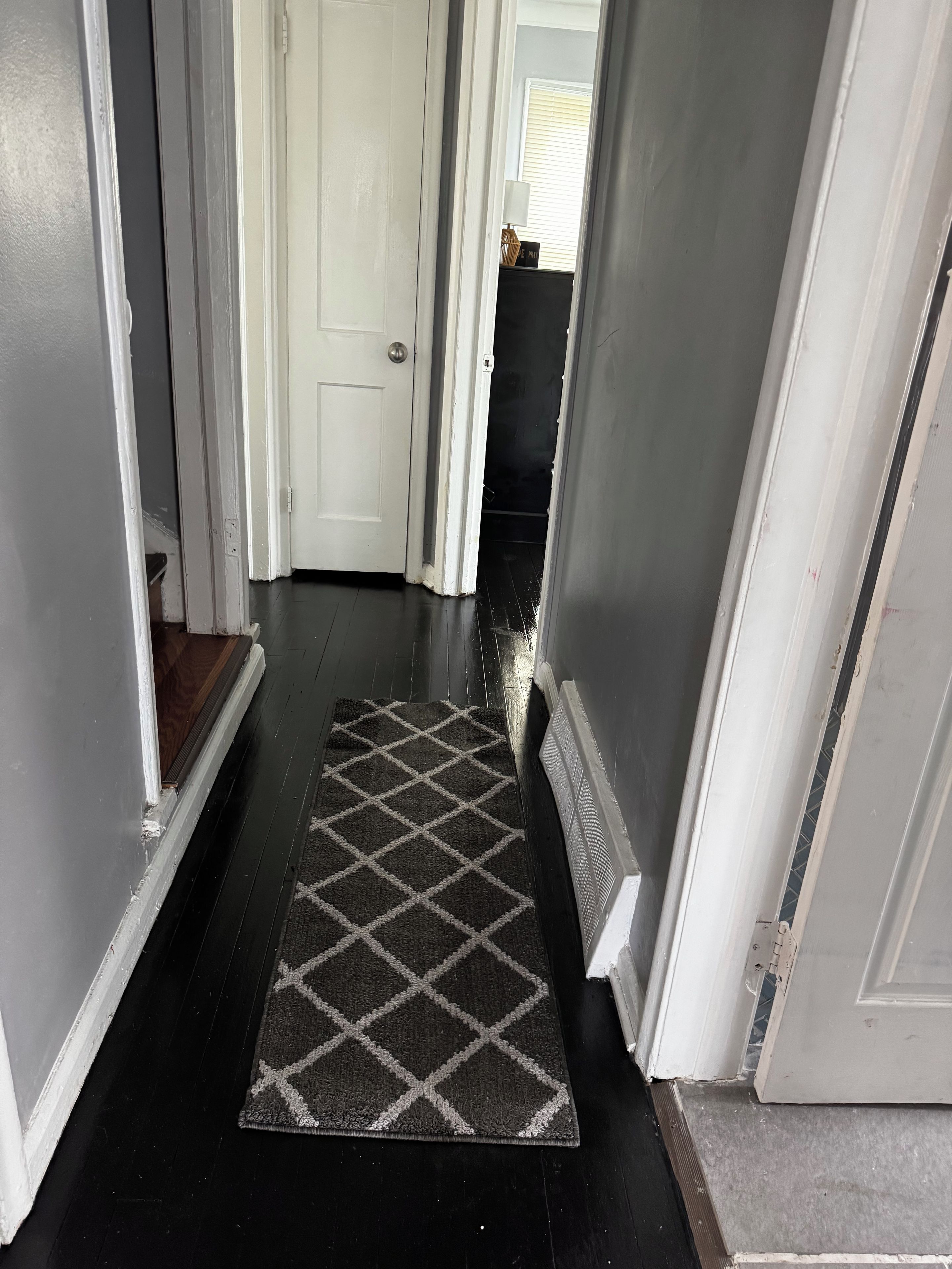 A hallway with a dark wooden floor, a patterned rug, and white walls.
