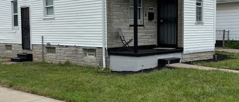 A single-story white house with a black roof, a front porch, and a stone foundation.