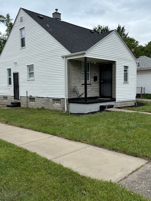 A single-story white house with a black roof, a front porch, and a stone foundation.