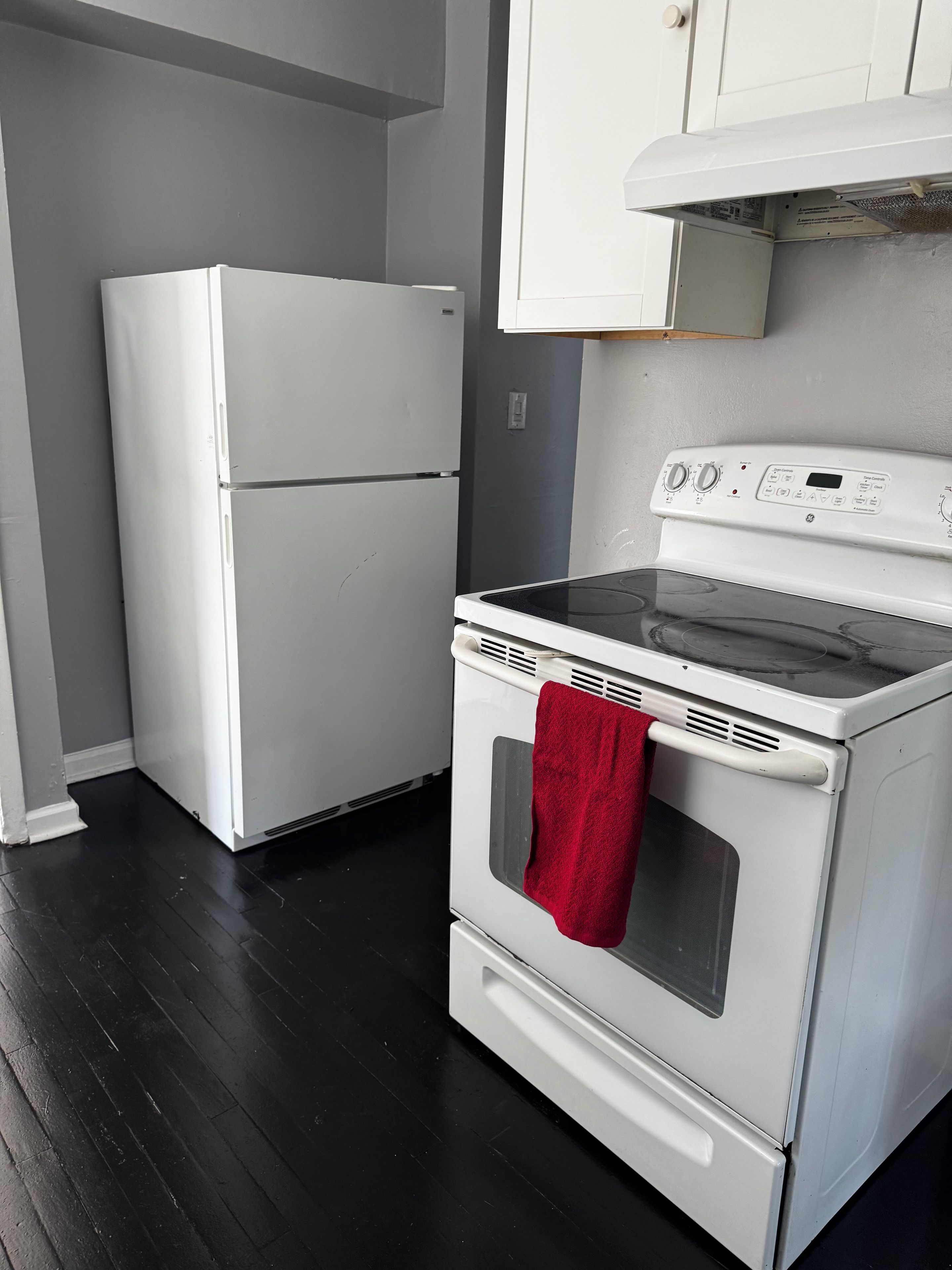 A kitchen with a white refrigerator, a white stove with a red towel, and grey walls.