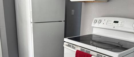 A kitchen with a white refrigerator, a white stove with a red towel, and grey walls.