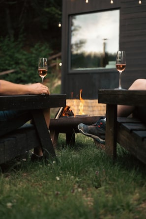Two people seated at wooden tables with a fire between them, outdoors. - Intimate cozy cabin with hot tub in Apuseni Mountains (Mătișești)
