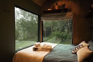 A bedroom with a large window, a bed with towels, and a view of a forest. - Intimate cozy cabin with hot tub in Apuseni Mountains (Mătișești)