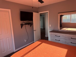 A bedroom with a bed, a dresser, a television mounted on the wall, and a window. - The cozy little house. (Fort Lauderdale)