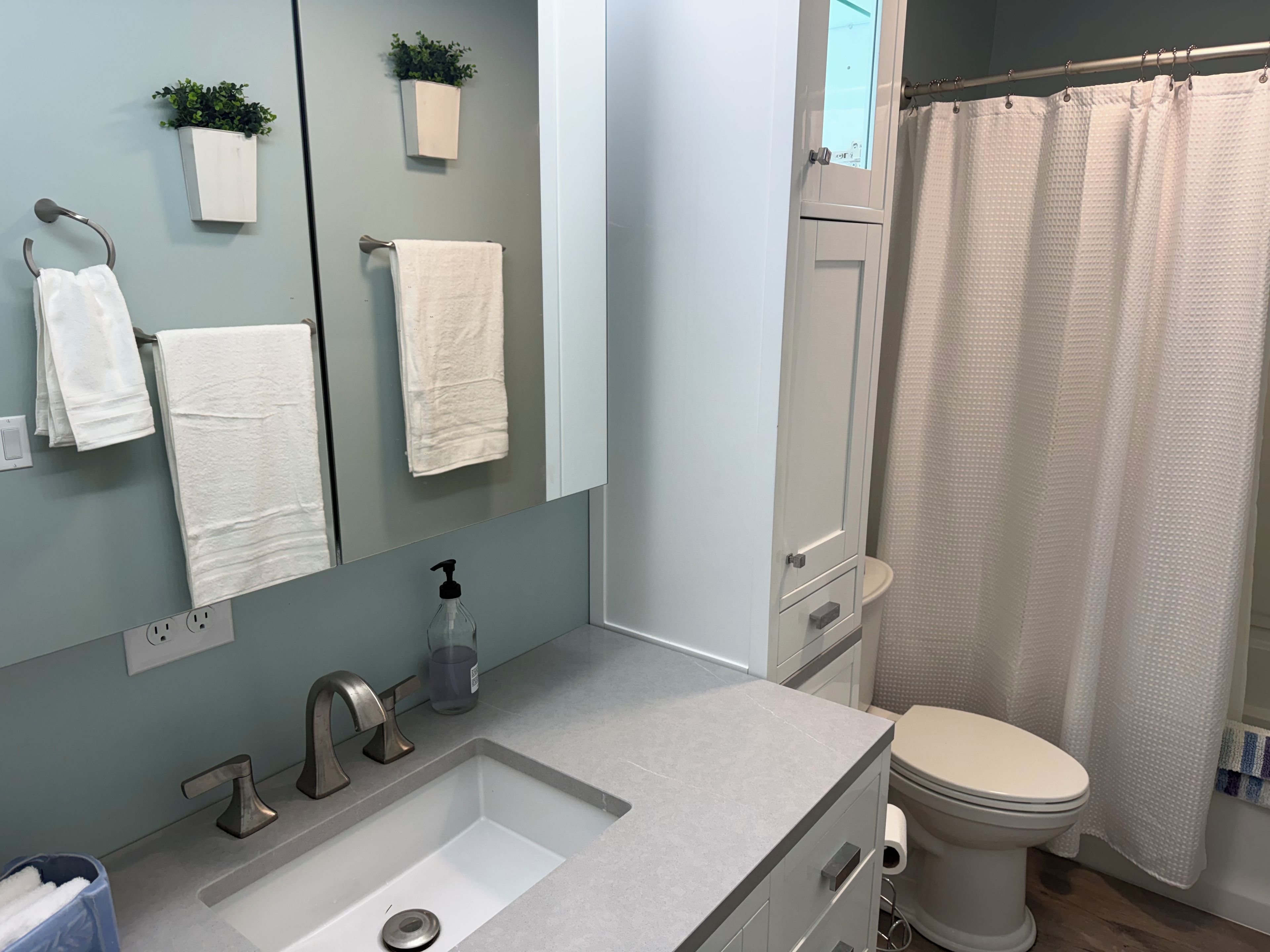 Un baño con lavamanos, espejo, toallero y retrete.