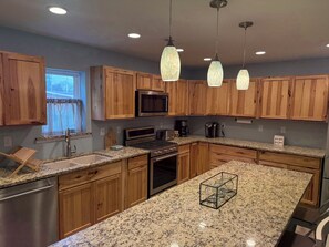 A kitchen with wooden cabinets, granite countertops, stainless steel appliances, and pendant lighting.