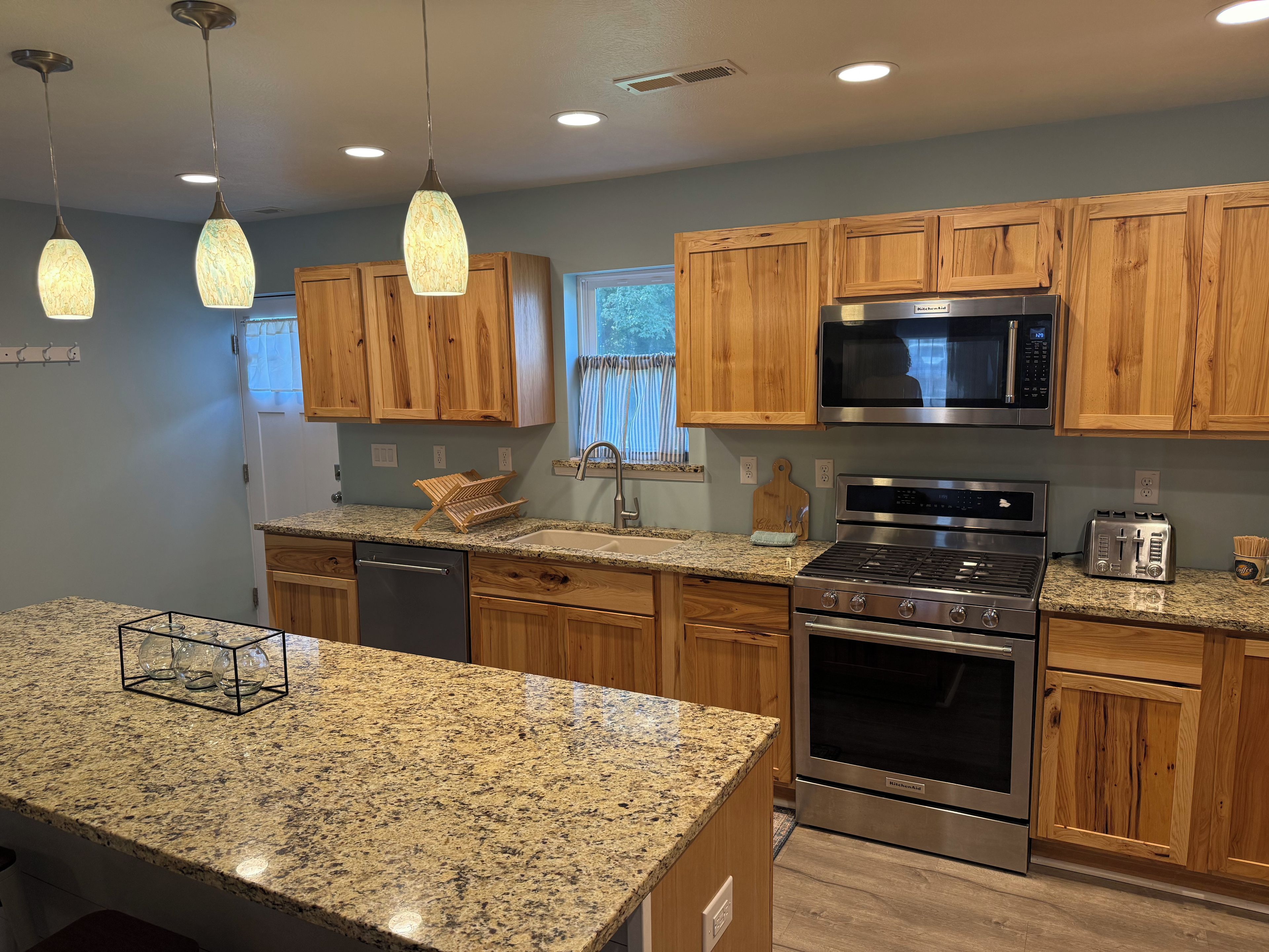 Una cocina con armarios de madera, encimeras de granito, estufa de acero inoxidable, microondas y luces colgantes.