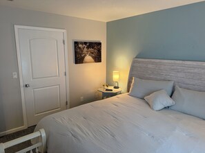 Een slaapkamer met een bed, een nachtkastje met een lamp, een deur en een aan de muur hangend schilderij.