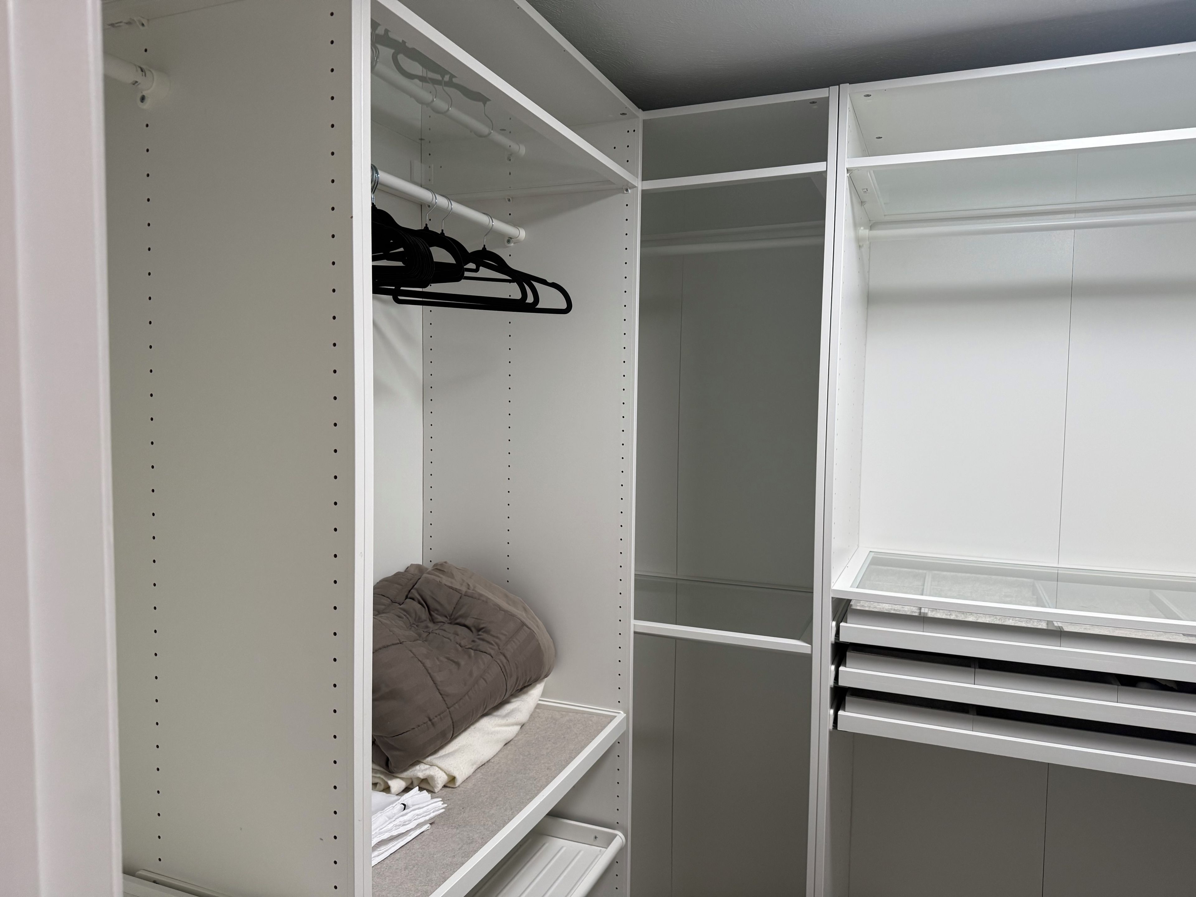 Um closet espaçoso com prateleiras abertas, cabideiro e uma cama com edredom marrom.