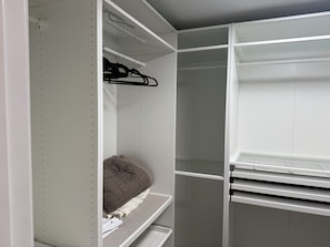 A walk-in closet with open shelves, a hanging rod, and a bed with a brown comforter.