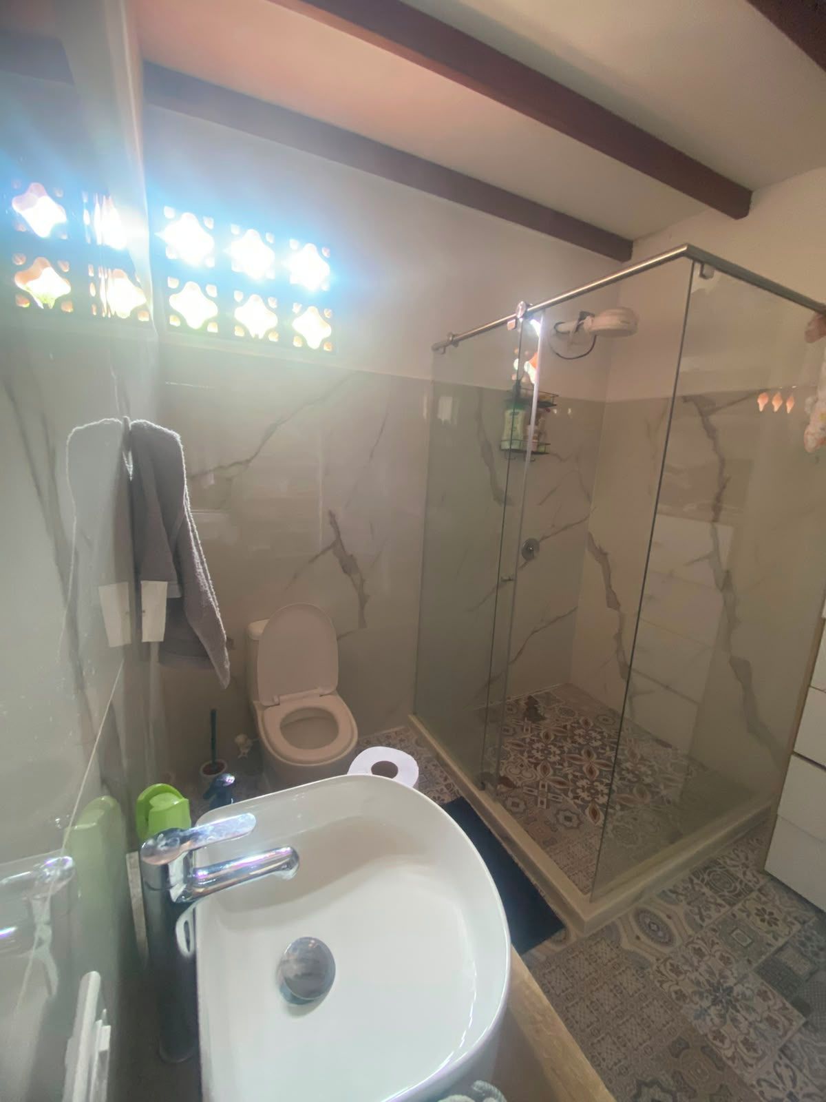 A bathroom with a glass-enclosed shower, a white sink, and a toilet.