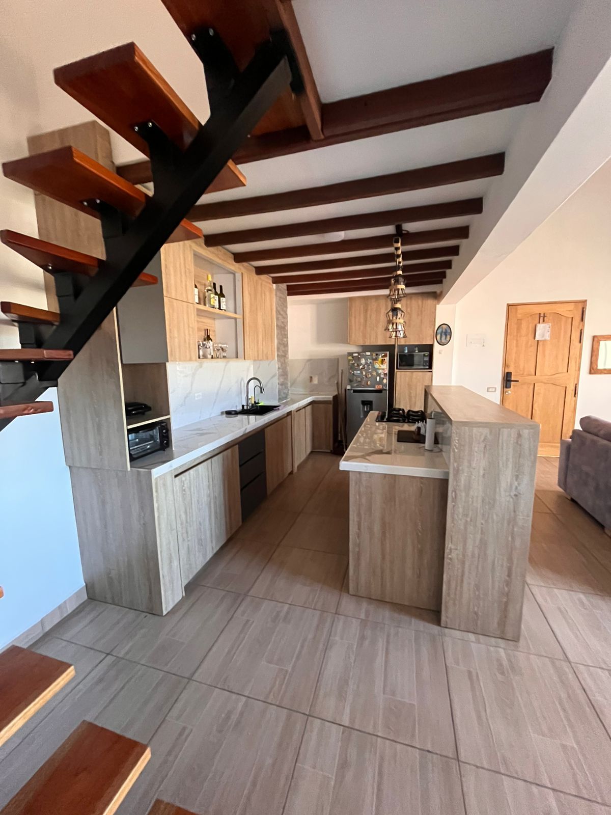 Une cuisine moderne dotée d’un îlot central, de poutres en bois au plafond et d’un four encastré.