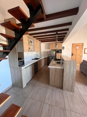 A modern kitchen with a central island, wooden beams on the ceiling, and a built-in oven.