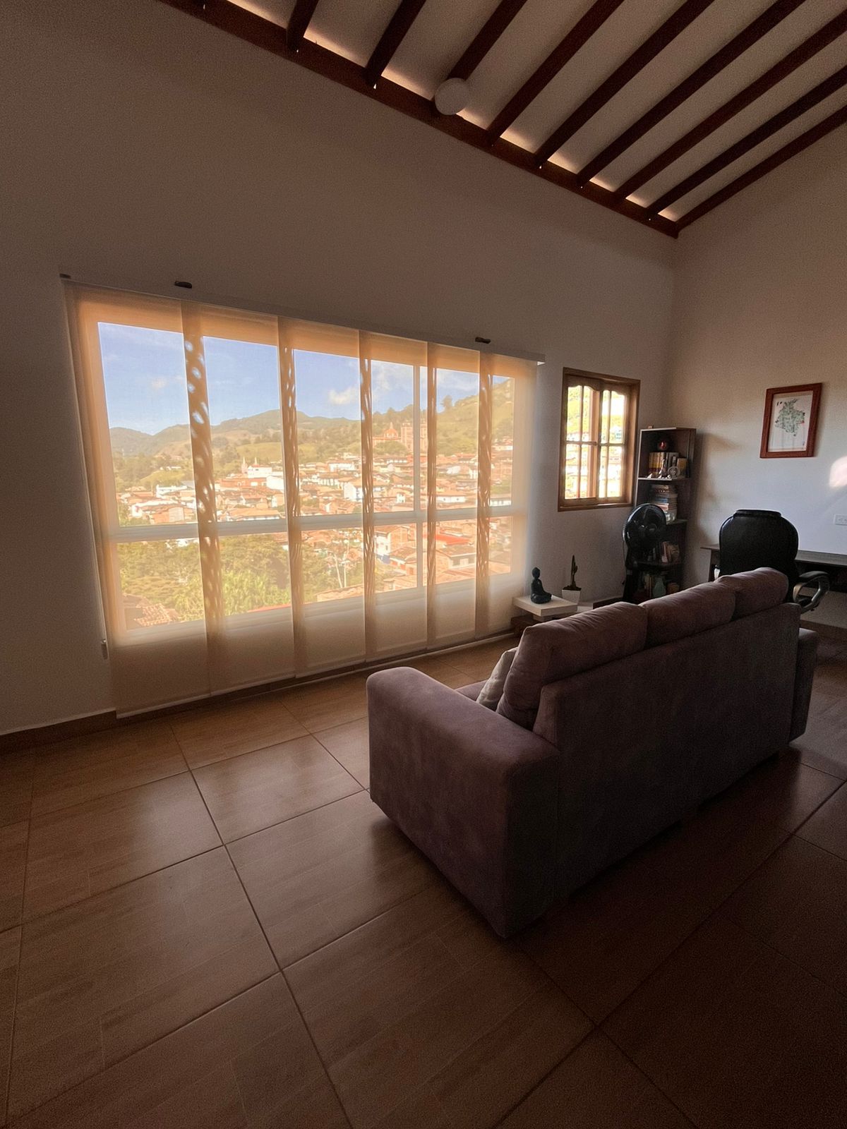 Un salon avec une grande fenêtre, un canapé et un ventilateur.