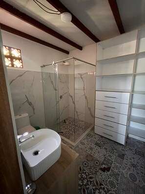 Un bany amb dutxa trencada per un envidriall, un lavabo blanc i terres amb rajoles estampades.