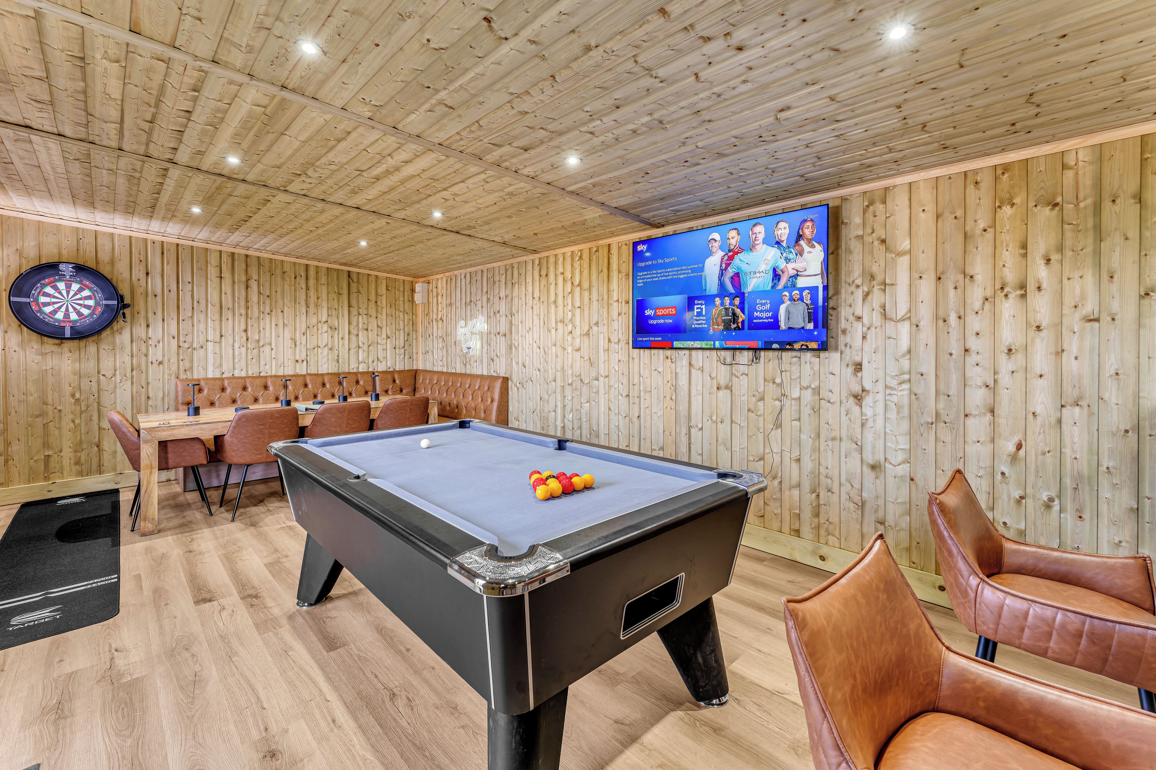 A billiards table with a pool cue, a dartboard, and a television screen displaying sports content.