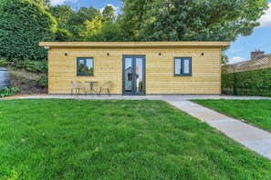 A small wooden cabin with a door, two windows, and a small patio with a table and chairs. - 31 Old Chester Road (Helsby)