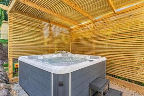 A hot tub under a wooden pergola with a stone wall and a small wooden stool. - 31 Old Chester Road (Helsby)