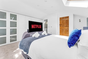 A modern bedroom with a large bed, a television mounted on the wall, and a wardrobe with sliding doors. - 31 Old Chester Road (Helsby)