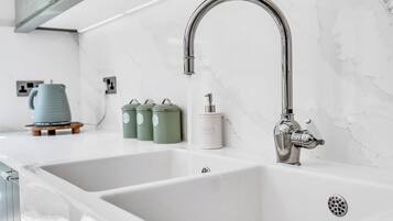 A modern kitchen with two white sinks, a stainless steel faucet, and a marble backsplash.