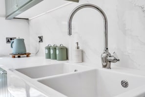 A modern kitchen with two white sinks, a stainless steel faucet, and a marble backsplash. - 31 Old Chester Road (Helsby)