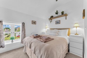 A bedroom with a bed, bedside lamps, a window with curtains, a radiator, and a small shelf with plants. - 31 Old Chester Road (Helsby)