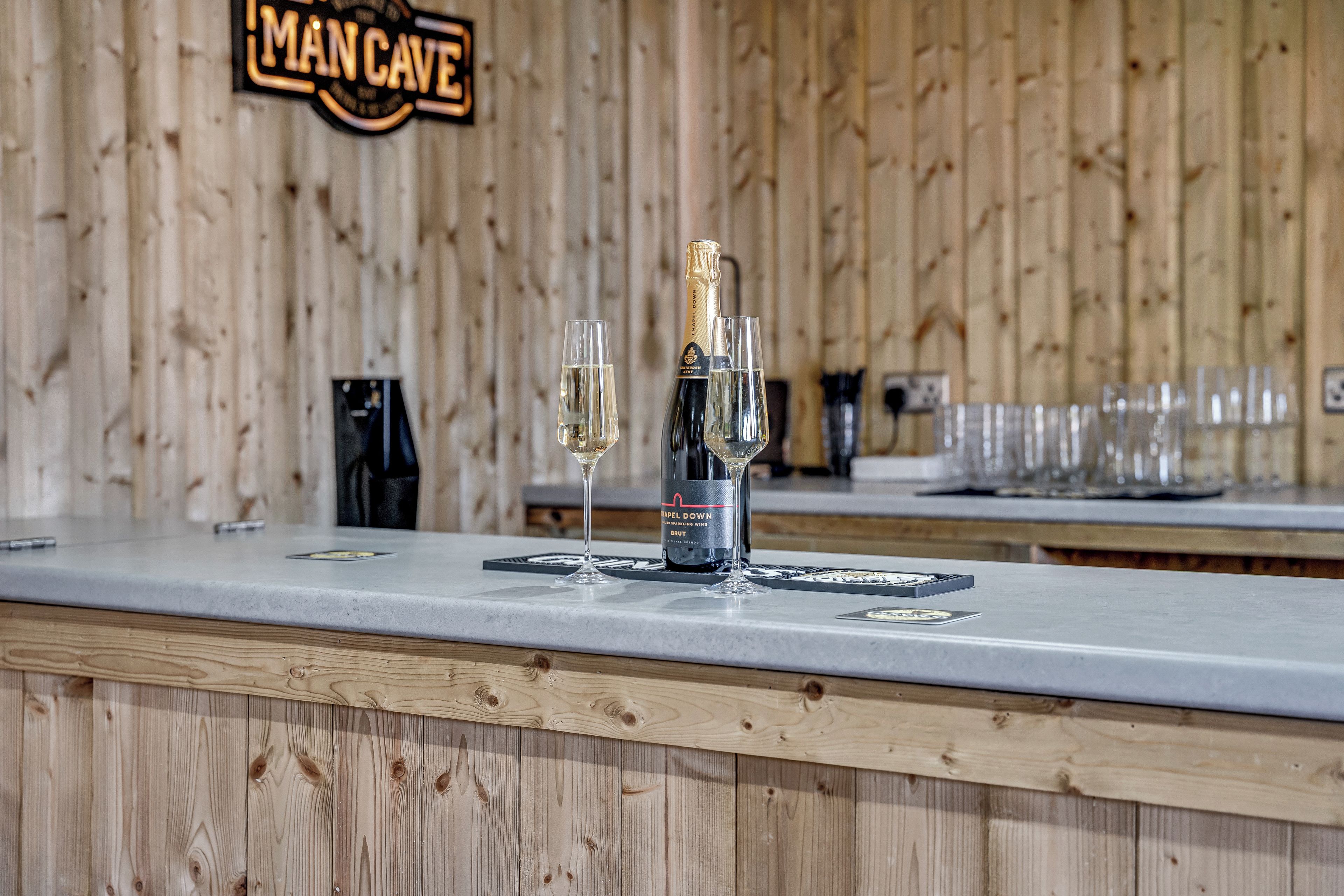 A bar area with a wooden backdrop, a bottle of champagne, and two glasses on a counter.