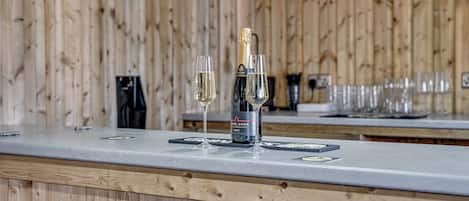 A bar area with a wooden backdrop, a bottle of champagne, and two glasses on a counter.