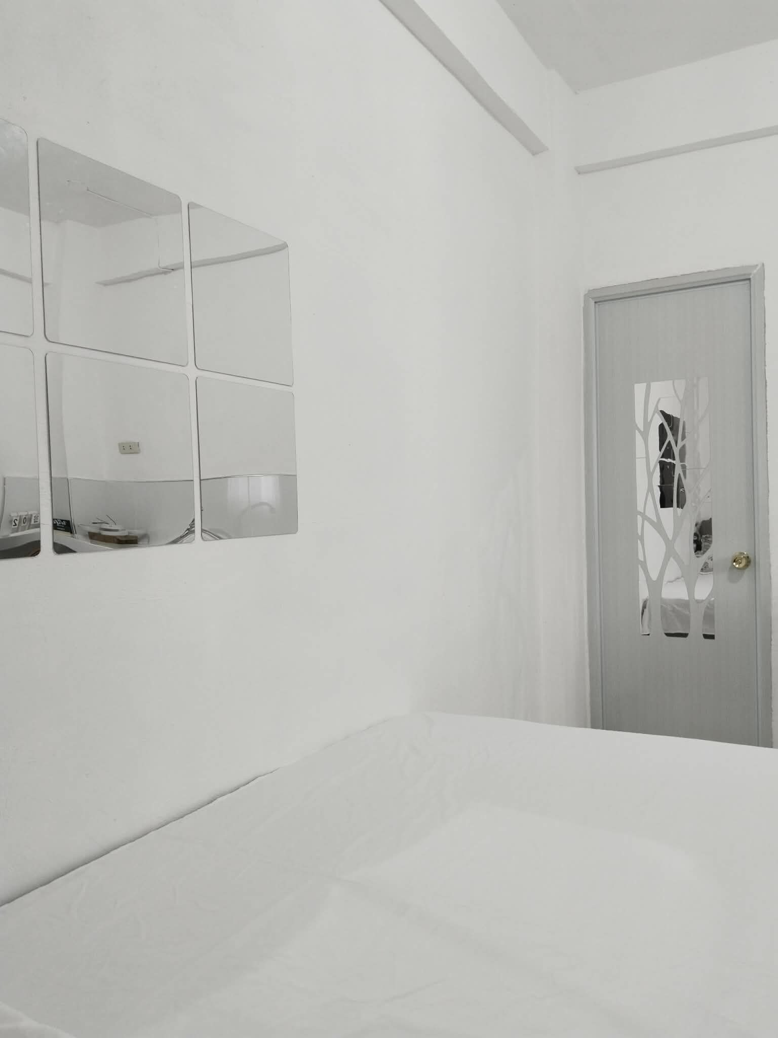 Une chambre à coucher au style minimaliste, avec un lit, un miroir fixé au mur et une porte ornée d’un motif décoratif.