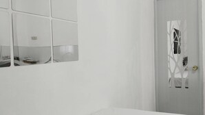 A minimalist bedroom with a bed, a wall-mounted mirror, and a door with a decorative pattern. - JNT Apartment is newly renovated studio with modern CR, w/ huge parking  space. (Pili)