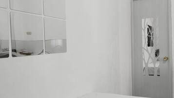 Une chambre à coucher au style minimaliste, avec un lit, un miroir fixé au mur et une porte ornée d’un motif décoratif.