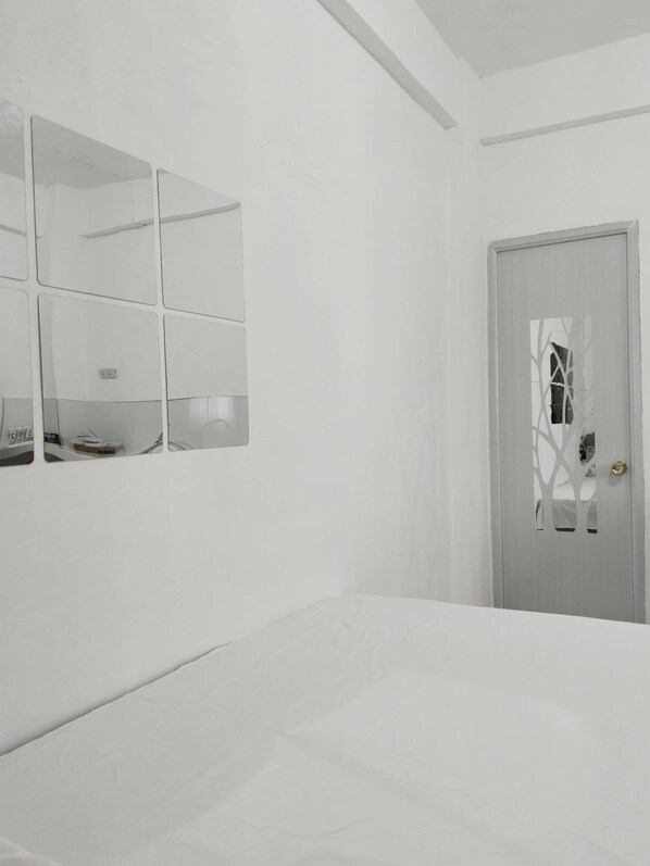 A minimalist bedroom with a bed, a wall-mounted mirror, and a door with a decorative pattern.