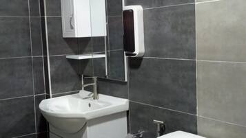 A modern bathroom with a white sink, mirror, toilet, and a small trash bin.