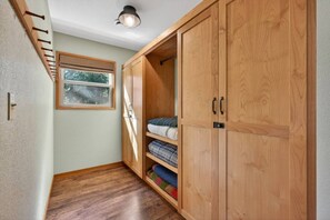 Ein Flur mit Holzdielen, einem Fenster mit Jalousien und einem Kleiderschrank mit mehreren Einlegeböden.