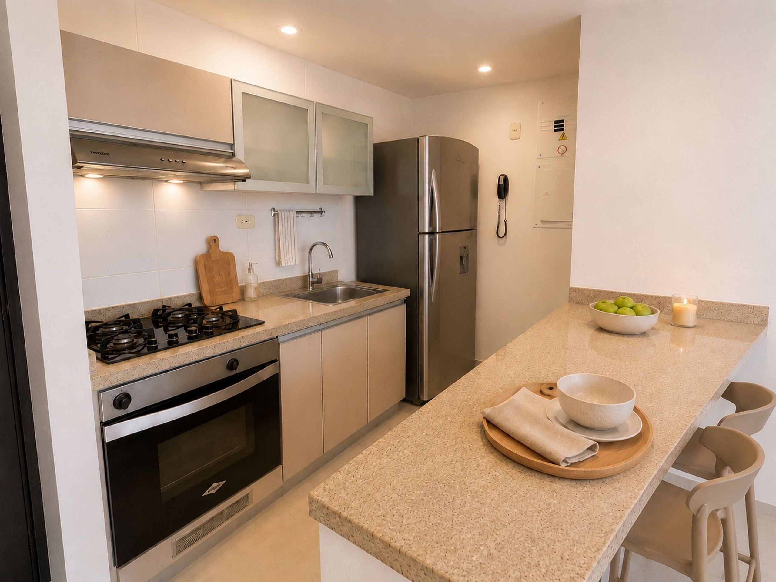 A modern kitchen with stainless steel appliances, a granite countertop, and a small dining area with chairs.