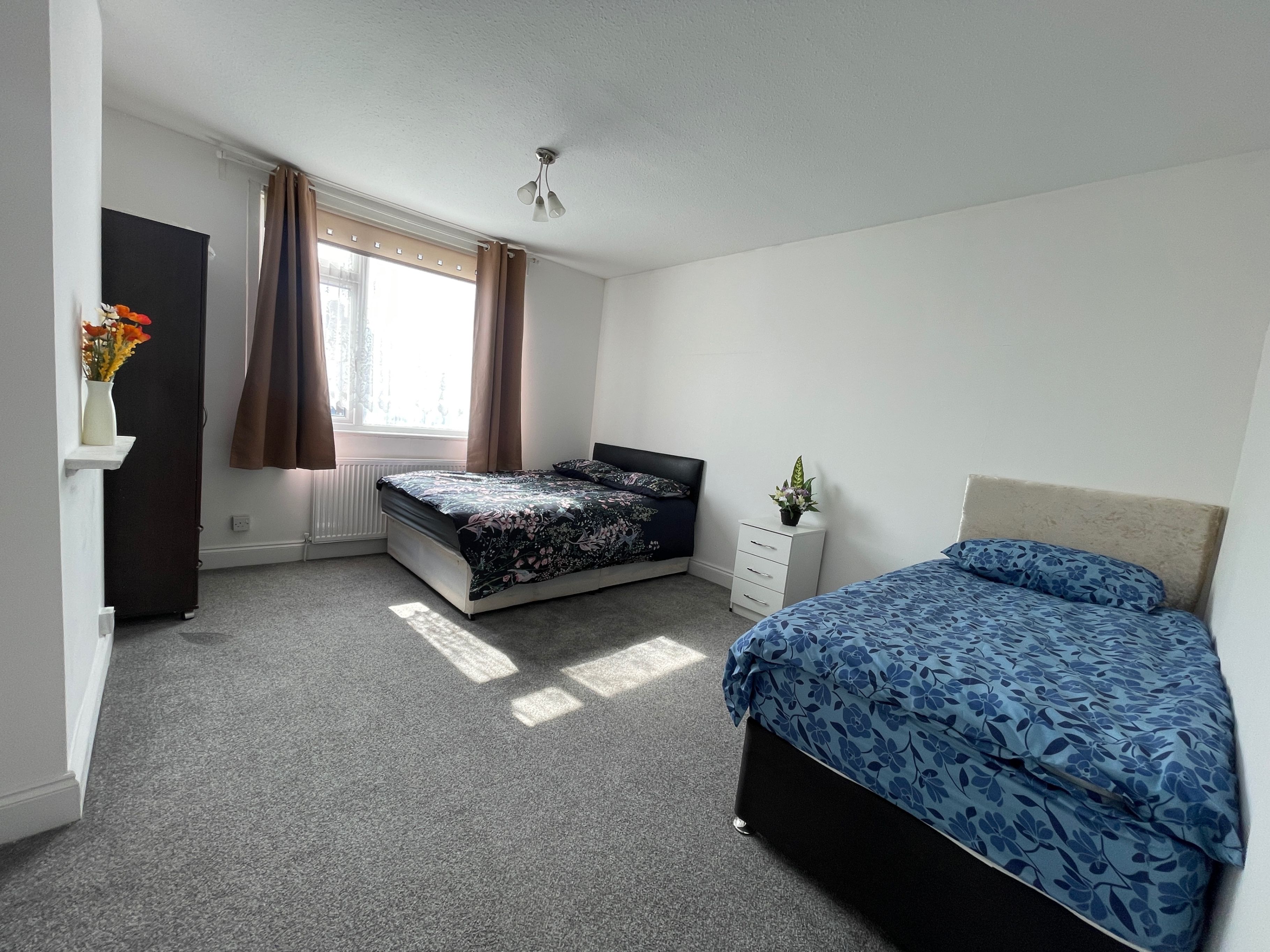 Een slaapkamer met een bed, een dressoir, een radiator en een raam met gordijnen.