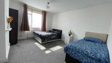 Een slaapkamer met een bed, een dressoir, een radiator en een raam met gordijnen.