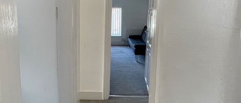 A narrow hallway with a carpeted floor leading to a room with a window and a bench.