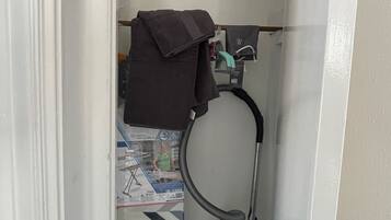 A small, narrow room with a door, a vacuum cleaner, and a hanging towel.