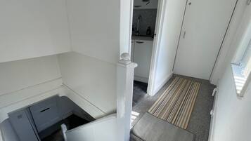 Una scala conduce a una zona cucina con una porta bianca e una pianta in vaso appesa al muro.