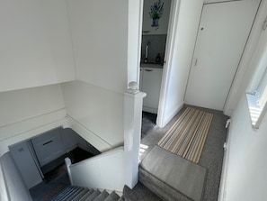A staircase leading to a kitchen area with a white door and a potted plant on the wall. - 1 Bedroom Apartm Sleeps 3 Driveway Near Leagrave T (Luton)