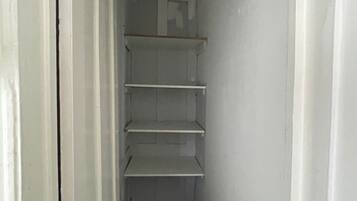 A narrow hallway with white walls and a door on the left. Shelves are mounted on the wall, and the floor is dark.