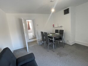 A dining area with a table set for four, four chairs, a clock on the wall, and a door leading to another room. - 1 Bedroom Apartm Sleeps 3 Driveway Near Leagrave T (Luton)
