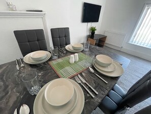 Uma sala de jantar com mesa posta para quatro, incluindo pratos, talheres e copos.