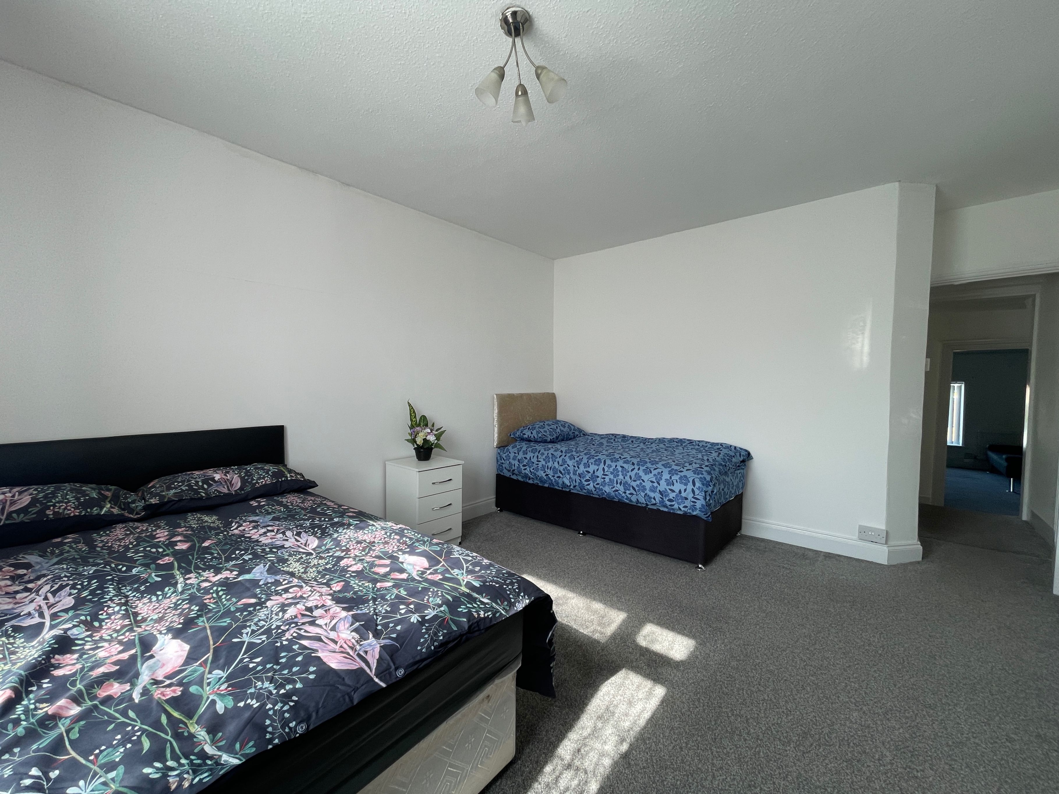 A bedroom with two beds, a nightstand, a ceiling fan, and a door leading to another room.