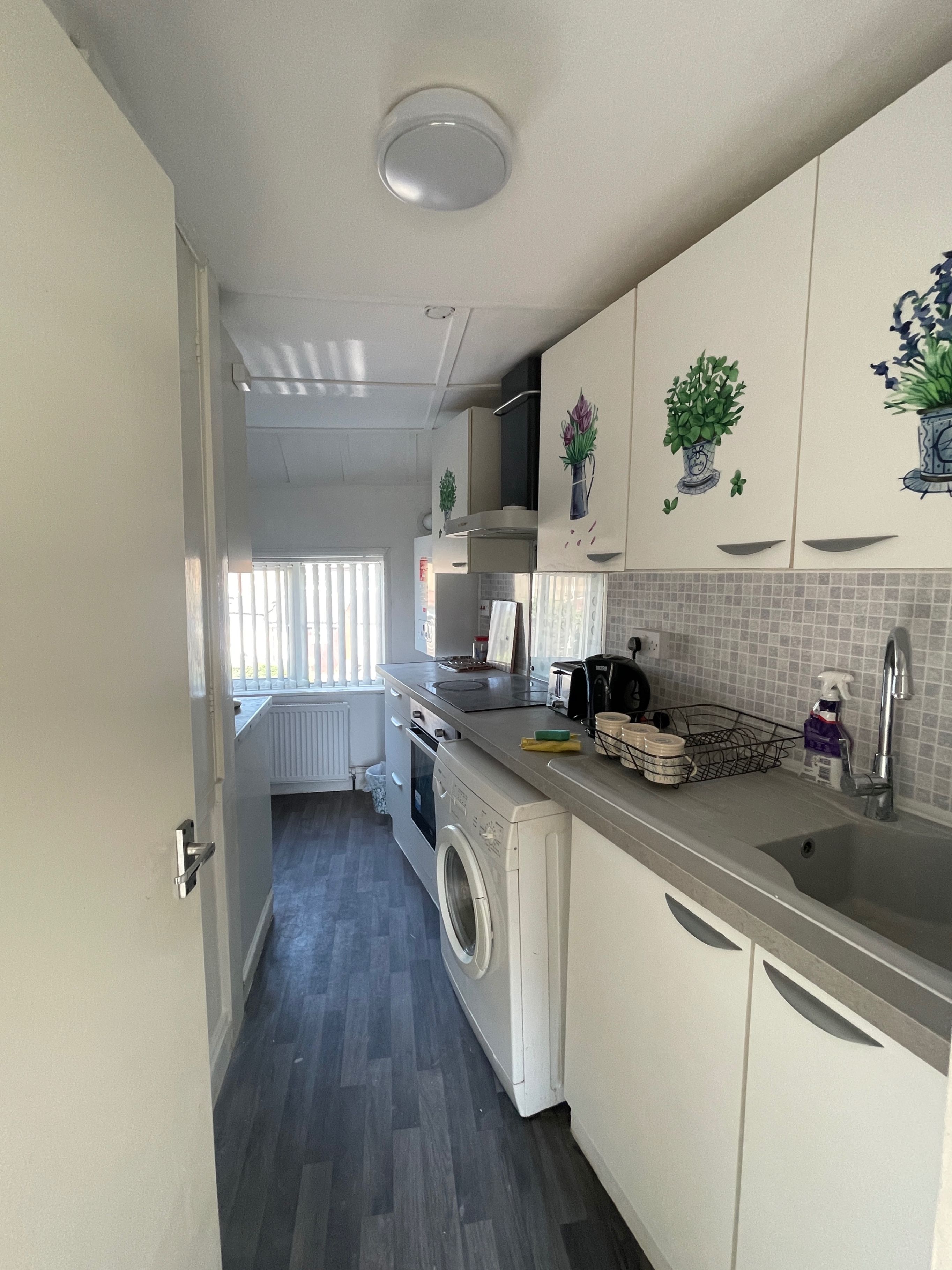 Een kleine keuken met een wasmachine, een koffiezetapparaat en een spoelbak.