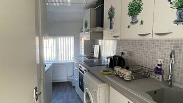 Een kleine keuken met een wasmachine, een koffiezetapparaat en een spoelbak.