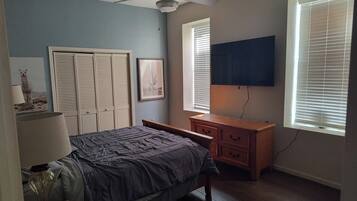 A bedroom with a bed, a desk, a ceiling fan, and a window with blinds.