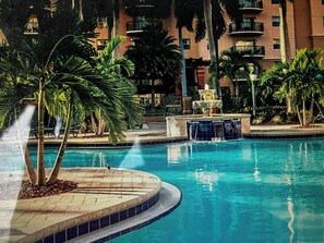A swimming pool with a fountain, surrounded by palm trees and a building with balconies. - Club Wyndham Palm-Aire 2 Bedroom, 2 Bath - Pampering Encouraged! (Pompano Beach)