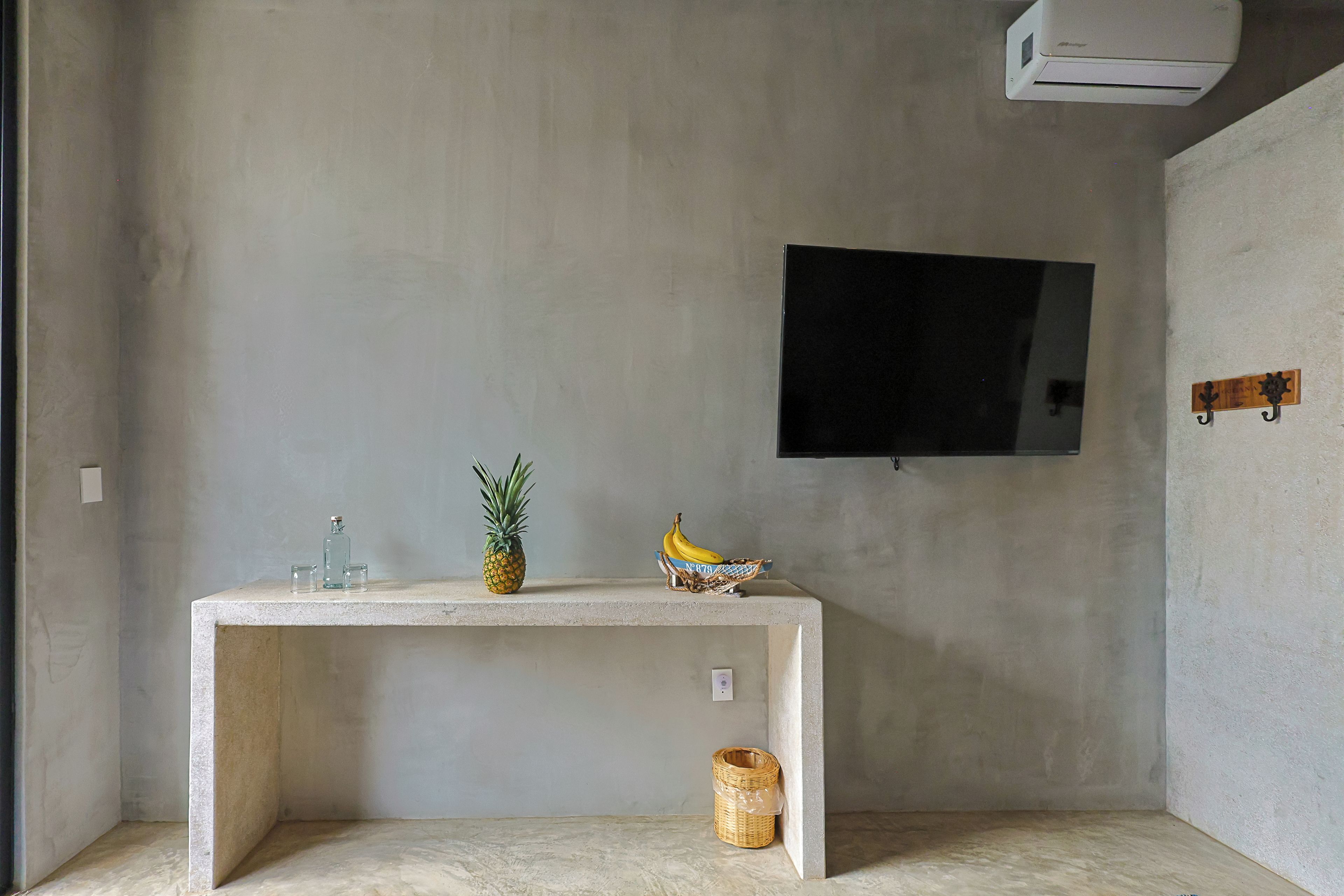 A room with a concrete table, a television mounted on the wall, and a small wicker basket.